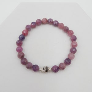 May include: A beaded bracelet featuring faceted, round beads in shades of pink and purple. The bracelet is strung on an elastic band and has a silver-colored clasp. The beads are approximately 8mm in diameter.
