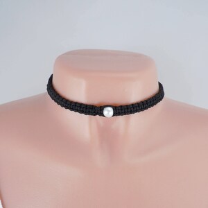 May include: A black braided choker necklace with a single white pearl accent.
