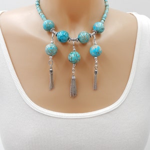 Pu&ograve; includere: Una collana statement turchese e argento con grandi perle rotonde e nappe pendenti. La collana &egrave; realizzata con pietre turchesi e metallo argentato.