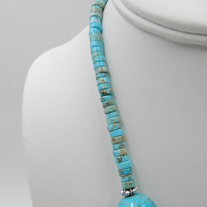 Pu&ograve; includere: Una collana turchese e argento con un grande ciondolo rotondo di turchese in basso. La collana &egrave; composta da piccole perle quadrate di turchese.