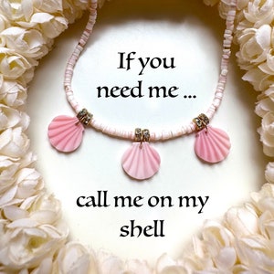 Puede incluir: Un collar de conchas blancas con colgantes de conchas rosas y diamantes de imitaci&oacute;n. El collar est&aacute; rodeado de una guirnalda de flores blancas. El texto "Si me necesitas... ll&aacute;mame a mi concha" est&aacute; escrito debajo del collar.