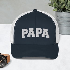 May include: A navy blue and white trucker hat with the word "PAPA" embroidered in white on the front.