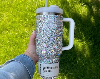 May include: A white stainless steel Stanley Quencher H2.0 Tumbler with a white handle and a straw. The tumbler is covered in iridescent rhinestones. The text on the tumbler reads "The Flowstate Quencher H2.0 Tumbler 40 oz | 1.18 L All Day Hydration."