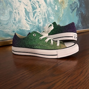 May include: Green, purple and gold glitter Converse trainers with white laces and a white rubber sole. The shoes have the Converse logo on the side.