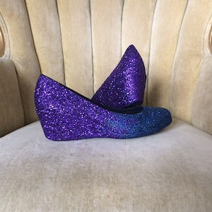 May include: A pair of purple and blue glitter wedge shoes. The shoes have a pointed toe and a wedge heel.