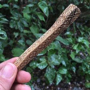 May include: A wooden stick with a carved geometric pattern. The stick is brown and has a light brown pattern.
