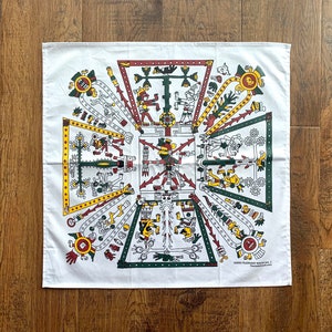 Puede incluir: Bandana de algodón blanco con un diseño azteca colorido que presenta patrones geométricos, figuras estilizadas y una cruz central. La bandana tiene una combinación de colores rojo, amarillo, verde y negro.
