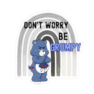 May include: A sticker featuring a grumpy blue bear with crossed arms, set against a gray and white rainbow. The text reads "DON'T WORRY BE GRUMPY" in black and blue lettering. The bear has a cloud with hearts and rain drops on its belly.