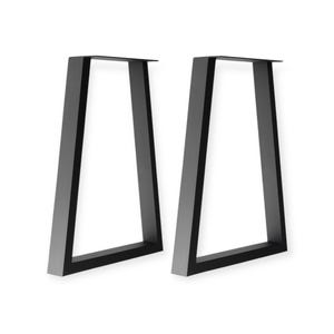 May include: Two black metal table legs with a trapezoid design. The legs are angled and have a flat top with a small lip for attaching to a tabletop. The legs are a matte black finish and are set against a white background.