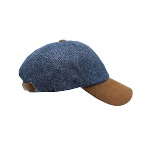 May include: A blue herringbone pattern cap with a brown suede brim and a brown leather strap. The cap has a classic design and is suitable for various occasions.