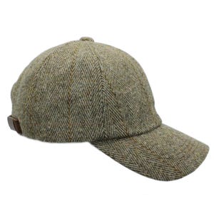 Puede incluir: Gorra de béisbol de tweed en tonos verdes, marrones y beige. La gorra presenta una visera curva y una correa de cuero marrón. La tela tiene un patrón de espiga.