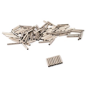 May include: A collection of small, silver metal tubes scattered on a white surface. Some tubes are grouped together, while others are spread out. The tubes appear to be hollow and cylindrical.