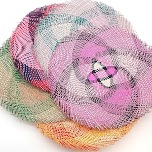 Może przedstawiać: Kolekcja kolorowych, tkanych podkładek w odcieniach różu, zieleni, czerwieni i żółci. Podkładki mają okrągły kształt ze spiralnym wzorem i są wykonane z teksturowanego materiału.