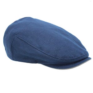 May include: A navy blue flat cap made from a textured fabric. The hat features a rounded crown and a small, stiff brim. The cap is a solid colour and appears to be made of a breathable material.