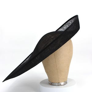 May include: A black hat with a wide brim, displayed on a mannequin head. The hat has a curved crown and a long, flat brim that extends outwards. The hat is made of a woven material, and the overall design is elegant and stylish.