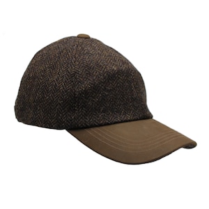 Puede incluir: Una gorra de béisbol con una corona de patrón de espiga en color marrón oscuro y una visera de color marrón sólido. La gorra tiene una forma de cúpula estructurada con un pequeño botón en la parte superior central y costuras visibles.