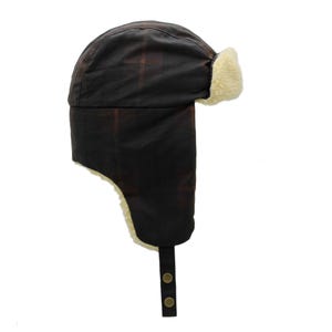 Könnte beinhalten: Dunkelbraune Trappermütze mit Karomuster. Die Mütze hat ein weiches, cremefarbenes Futter um Ohren und Gesicht sowie einen Kinnriemen mit zwei Knöpfen. Diese Wintermütze ist zum Schutz vor Kälte und Witterungseinflüssen konzipiert.