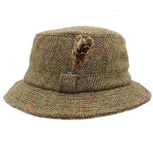 May include: A green, brown, and red tweed bucket hat with a herringbone pattern. The hat is adorned with a feather and has a band around the crown. The brim is slightly curved, typical of a classic style.