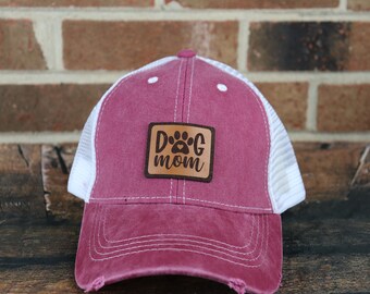 May include: A red and white trucker hat with a brown leather patch that says "Dog Mom" with a paw print and a heart.