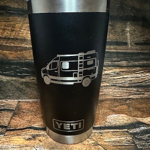 May include: Black Yeti tumbler with a laser engraved design of a camper van. The tumbler has a silver lid and base.