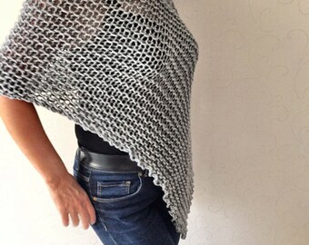 May include: A grey knitted poncho with a loose, open weave. The poncho is worn over a black top and blue jeans.