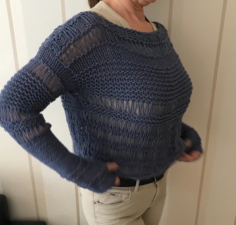 May include: A blue knitted sweater with a loose, open weave. The sweater has a round neckline and long sleeves.