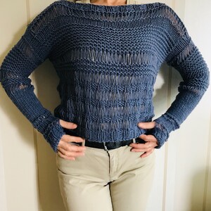 May include: A blue knitted sweater with a loose fit and long sleeves. The sweater has a textured pattern and a slightly open neckline.