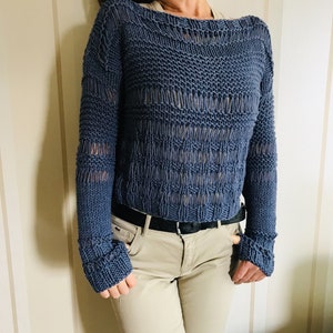 May include: A blue knitted sweater with a loose fit and openwork design. The sweater has long sleeves with a ribbed cuff detail.