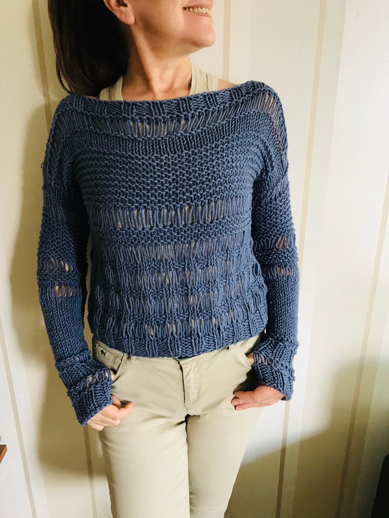 May include: A blue knitted sweater with a loose fit and openwork design. The sweater has a wide neckline and long sleeves.