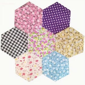 Può includere: Una composizione floreale di sette pezzi di tessuto esagonali. I tessuti presentano vari motivi, tra cui stampe floreali in rosa, giallo e blu, pois viola e un motivo a scacchi bianco e nero. La disposizione è su sfondo bianco.