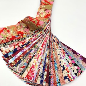 May include: A collection of Japanese washi paper strips in a fan arrangement. The strips display a range of patterns, including florals and waves, in colours such as red, blue, and gold. Each strip is approximately 1 cm wide, showcasing the intricate designs.