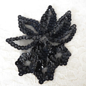 May include: Black sequined flower applique. The sequins are arranged in a flower shape with a mesh backing.