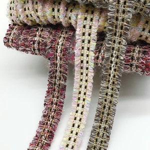 May include: Three different types of woven trim with a textured, fringed edge. The trim is black, white, and pink with gold accents.