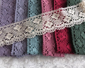 Op de afbeelding: Assortiment van kantbies in verschillende kleuren, waaronder paars, teal, roze, rood en groen. De kant is delicaat en heeft een bloemenpatroon.