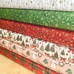 May include: A stack of six fabric bolts featuring holiday patterns. The top bolt is white with gold and silver stars. Below are green and red bolts with gold floral patterns, followed by cream, pink, and plaid bolts with Christmas motifs.