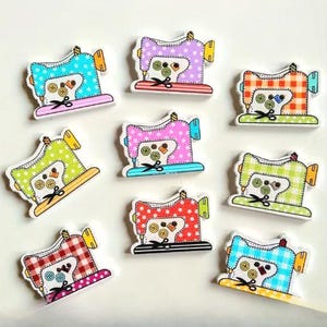 May include: Nine colourful wooden sewing machine buttons. Each button features a different colour scheme, including blue, green, pink, red, and purple. The buttons have a white outline and include details like scissors and buttons.