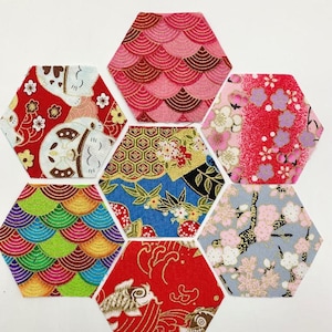 Op de afbeelding: Een verzameling van zeven zeshoekige stoffen patches met Japanse patronen. De patches tonen verschillende ontwerpen, waaronder golven, bloemmotieven en een gelukskat, in levendige kleuren zoals rood, roze, blauw en groen.
