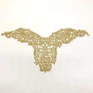 May include: Gold-coloured lace appliqué with an intricate, symmetrical design. The lace has a V-neck shape with detailed floral and scrollwork patterns. The appliqué is likely for embellishing clothing or craft projects.