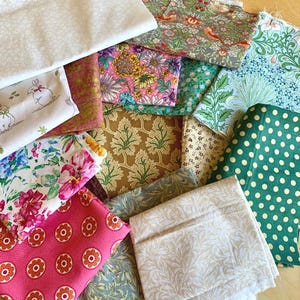 May include: A collection of assorted fabric swatches featuring various patterns including floral prints, polka dots, botanical motifs, and a white rabbit design in colours such as pink, green, blue, brown, and cream, layered together in a stack.