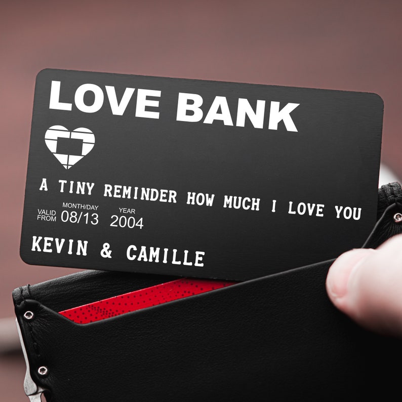 May include: A black metal card with the words "LOVE BANK" printed in white. The card has a small heart icon and the text "A TINY REMINDER HOW MUCH I LOVE YOU". It also includes the text "VALID FROM 08/13 2004 KEVIN & CAMILLE".