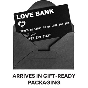 May include: A black card with the text "LOVE BANK" and the phrase "THERE'S NO LIMIT TO MY LOVE FOR YOU". The card also includes the date "05/27 2023" and the names "NFER AND STEVE". The card is in a black envelope. The text "ARRIVES IN GIFT-READY PACKAGING" is below the image.