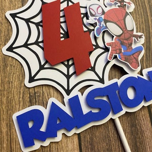 May include: A red number four, a blue name "RALSTON", and three Spiderman characters on a white spiderweb cake topper.