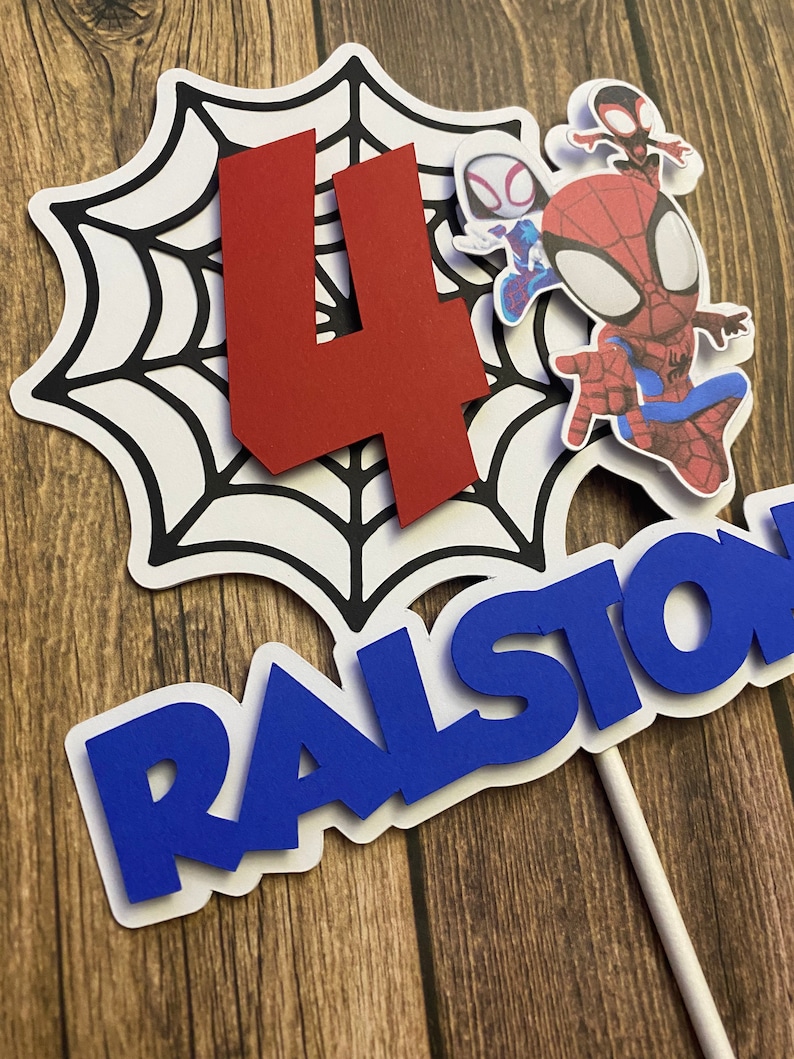 May include: A red number four, a blue name "RALSTON", and three Spiderman characters on a white spiderweb cake topper.