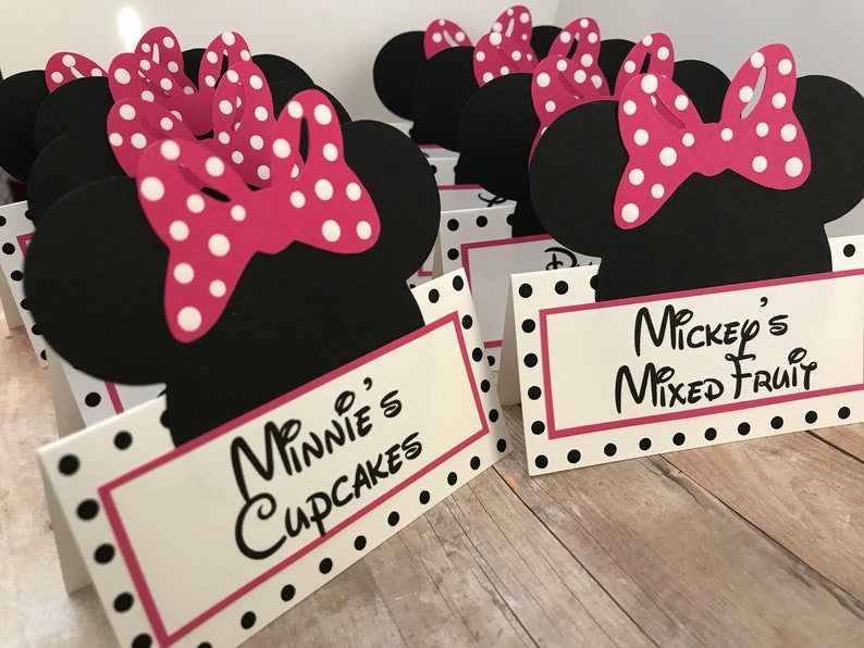 May include: Black and white Minnie Mouse themed table cards with pink polka dot bows. The cards have the text "Minnie's Cupcakes" and "Mickey's Mixed Fruit".