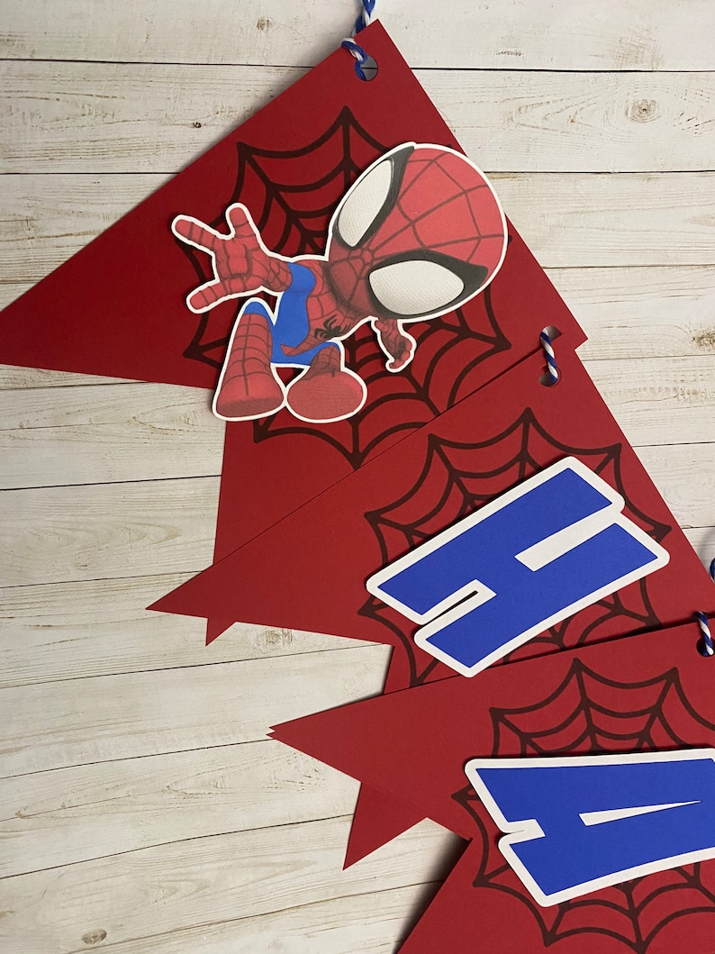 Puede incluir: Bandera roja y azul con un personaje de Spiderman y las letras 'Happy' en azul sobre un fondo rojo con un dise&ntilde;o de telara&ntilde;a negra.