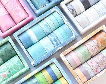 May include: Assortment of colorful washi tapes in various patterns and designs, organized in boxes. The tapes are arranged in rows and columns, showcasing a variety of textures and colors.