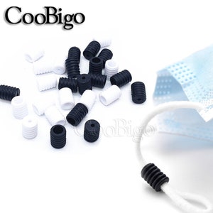 May include: A close-up of a pile of black and white silicone mask strap adjusters. The adjusters are small, cylindrical, and have a ribbed texture. There is also a white mask strap with a black adjuster on a blue mask.