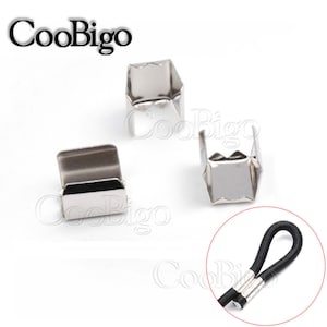 Puede incluir: Tres terminales de cordón de metal plateado con un primer plano de un terminal de cordón unido a un cordón elástico negro.