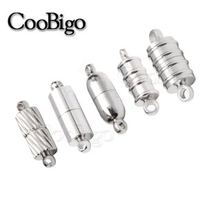 Puede incluir: Varios cierres magnéticos plateados para la creación de joyas. Los cierres presentan diversos diseños, lisos, acanalados y cilíndricos. Cada cierre tiene un lazo en cada extremo para sujetar a los componentes de la joya. La marca "CooBigo" es visible.