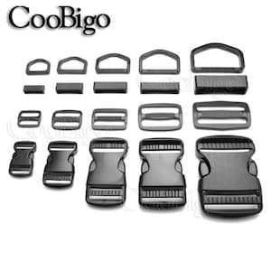 Op de afbeelding: Een set zwarte plastic gespen en glijders in verschillende maten. De gespen zijn rechthoekig met twee gaten en de glijders zijn rechthoekig met één gat. De gespen en glijders zijn in rijen gerangschikt.